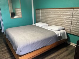 Un letto singolo con struttura in legno e testata imbottita, posizionato di fronte a pareti color acquamarina con uno specchio sopra.