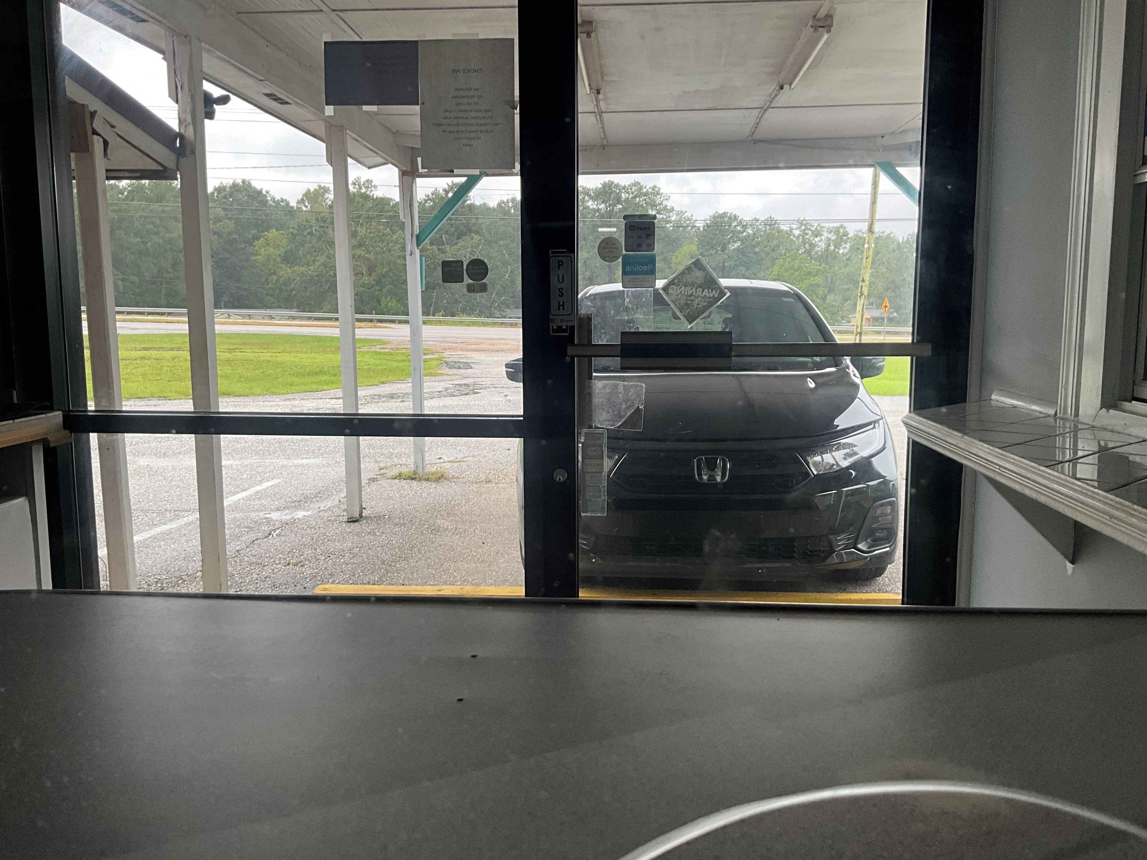 Een auto rijdt via een glazen deur een gebouw binnen, met een parkeerplaats op de achtergrond.
