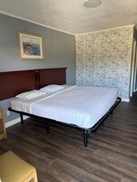 Un dormitorio con cabecera de madera, una cama grande con ropa de cama blanca, un cuadro en la pared y un papel tapiz estampado.
