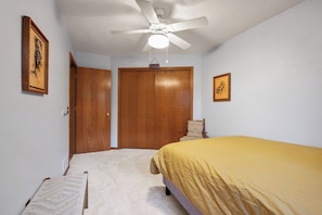 Ein Schlafzimmer mit einem Bett, Deckenventilator, einer Tür und einem Sessel.