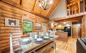 A log cabin interior with a dining area, kitchen, and a view of the outdoors. - Private Riverfront Cabin | Little Pigeon River (Pigeon Forge)