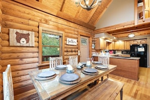 A wooden cabin interior with a dining table set for six, wooden walls, a kitchen area, and a sign that reads 'Gather'. - Private Riverfront Cabin | Little Pigeon River (Pigeon Forge)
