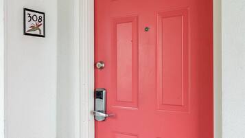 A red door with a silver handle and a keyhole, a small sign with the number 308, and a white wall.