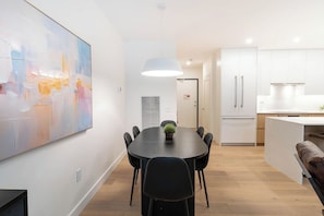 Een moderne keuken met witte kasten, een inbouwoven en een eethoek met een ronde tafel en zwarte stoelen.