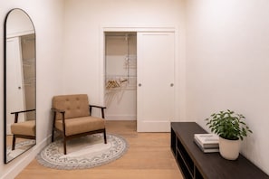 A room with a chair, a mirror, a wardrobe, a plant, and a small table. - Treeline Lodge - Townhome with Private Hot Tub (Revelstoke)