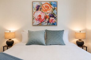A hotel room with a large bed, two bedside lamps, and a floral painting on the wall. - Treeline Lodge - Townhome with Private Hot Tub (Revelstoke)