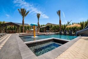 Une piscine avec un toboggan, entourée de palmiers et dotée d’un espace de repos abrité.