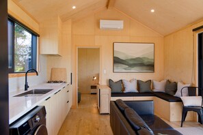 A compact living space with a kitchenette, a dining area, and a seating area with a sofa and cushions. - Bay Paddock - Kaikoura Holiday Home (Kaikoura)