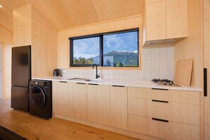 Eine moderne Küche mit Holzausstattung, einer integrierten Waschmaschine, einem großen Fenster mit Bergblick und einem schwarzen Kühlschrank.