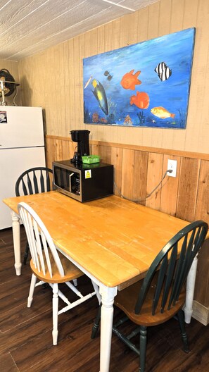 A dining area with a wooden table and chairs, a painting of fish on the wall, and a black appliance on the table. - BC7--Studio Sleeps 2 Adults/2 Kids, Walk to Beach, Pool/Hot Tub, Dogs OK! (Port Aransas)