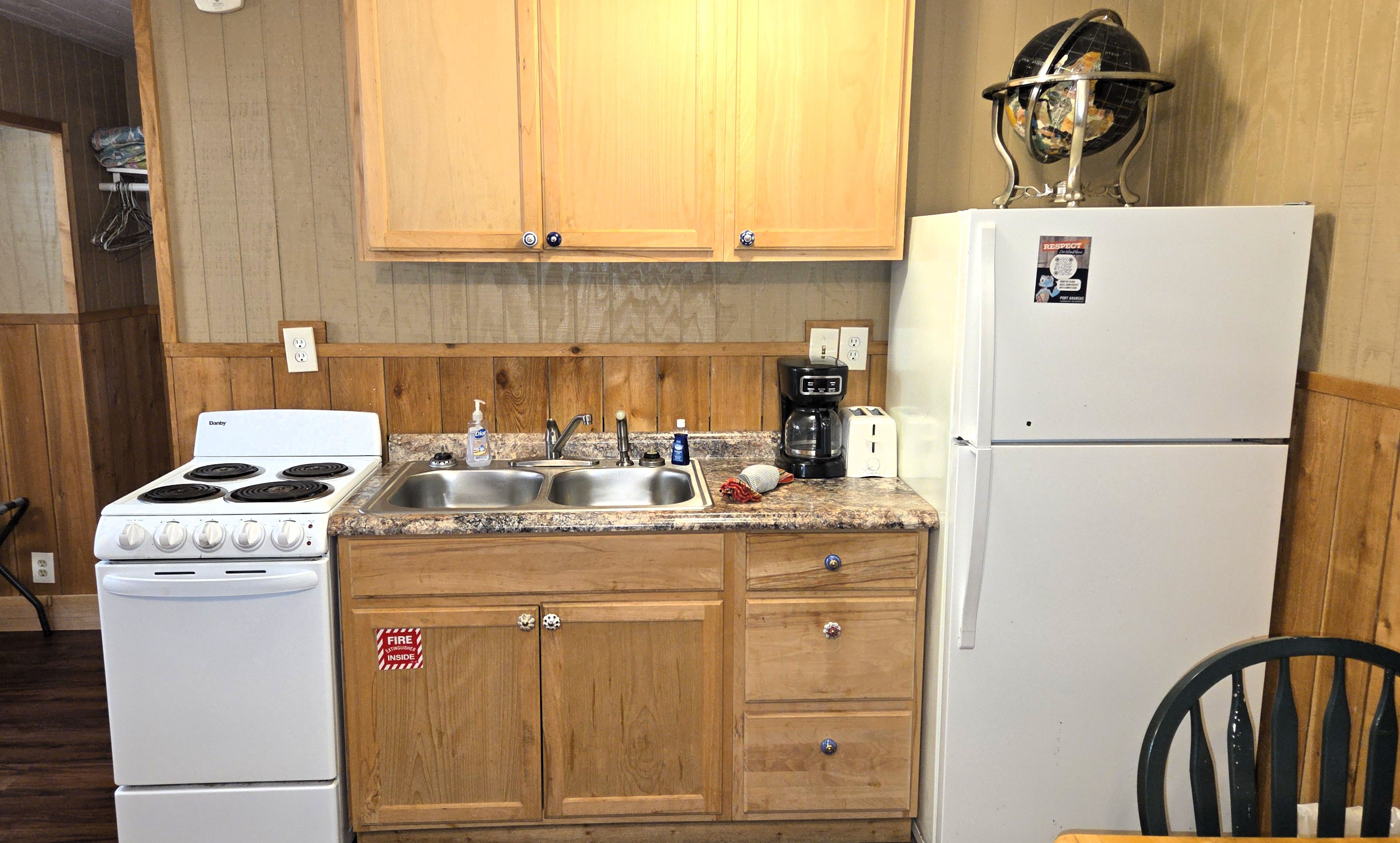 A kitchen with wooden cabinets, a stove, a sink, a coffee maker, and a refrigerator.