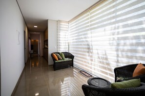 A hallway leading to a room with a wicker sofa and a chair, a large window with blinds, and a tiled floor. - Ch Cara com Piscina Hidro e Lago em Trindade - GO (Goiânia)