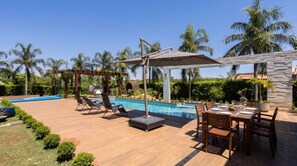 Ein Poolbereich mit Esstisch für vier Personen, Liegestühlen und einer Pergola mit Markise.