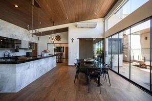 Eine moderne Küche mit Marmorarbeitsplatte, Holzboden und einem Essbereich mit Glastisch und Stühlen.