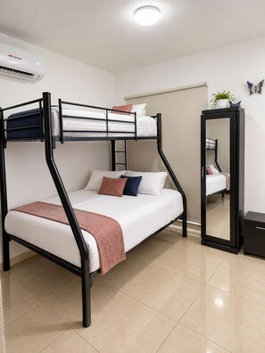 Een stapelbed met matras, kussens en een dekbed. Er hangt een spiegel aan de muur en op het nachtkastje staat een klein plantje.