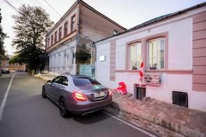 Un’auto parcheggiata in strada, con un edificio che presenta una finestra e una insegna con una bandiera rossa.