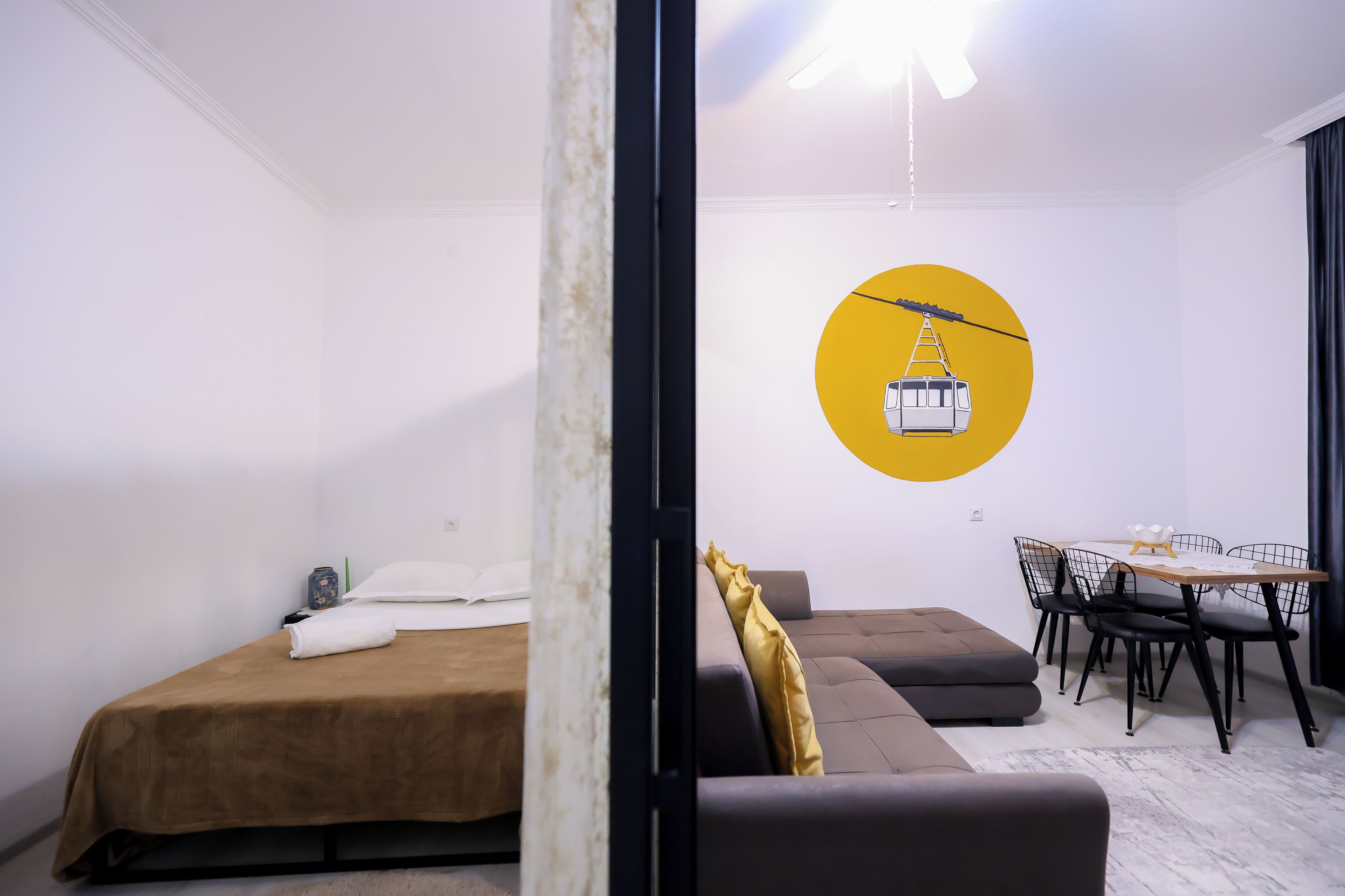 Um quarto moderno com cama, sofá, mesa de jantar com cadeiras e uma obra de arte pendurada na parede retratando um teleférico.