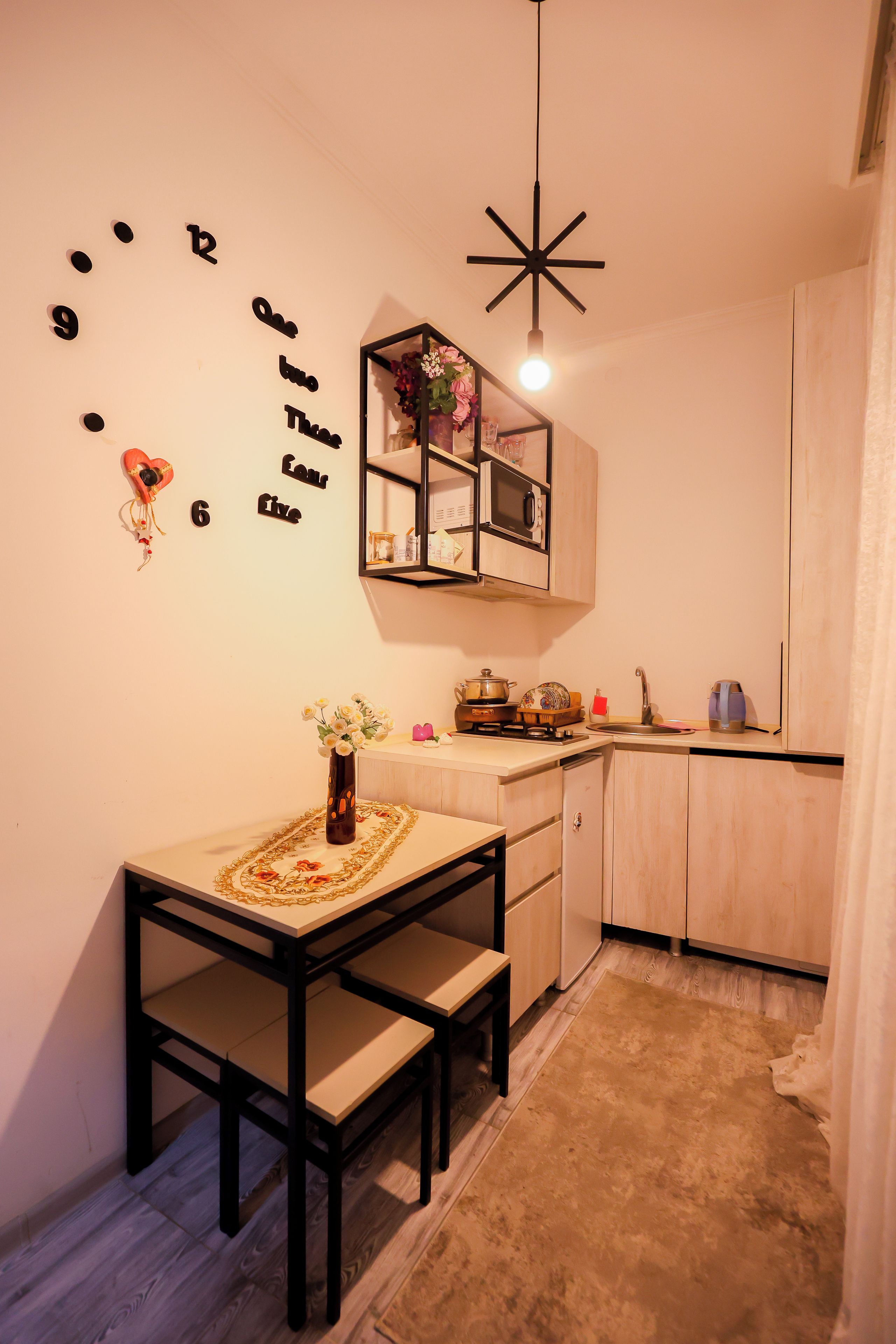 A compact kitchen with a dining area, a wall clock, and a hanging light fixture.