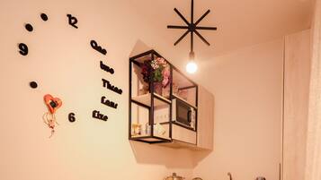 A compact kitchen with a dining area, a wall clock, and a hanging light fixture.