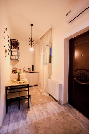 A compact kitchen with a dining table, a hanging light fixture, and a radiator.