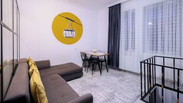 Una sala de estar moderna con un sofá, una mesa de comedor con sillas y un ventanal con cortinas.