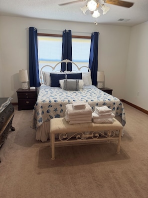 Ein Schlafzimmer mit einem Bett, Nachttischen, einer Bank, einem Schminktisch und einem Deckenventilator.