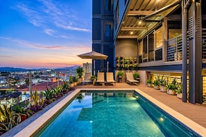 Piscina no terraço com vista para a paisagem urbana, espreguiçadeiras e plantas em vasos.