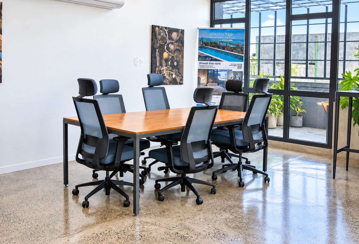 A conference room with a wooden table and black office chairs, large windows with a view, and a poster on the wall.