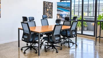 Une salle de conférence avec une table en bois et des chaises de bureau noires, de grandes fenêtres offrant une vue dégagée et une affiche accrochée au mur.