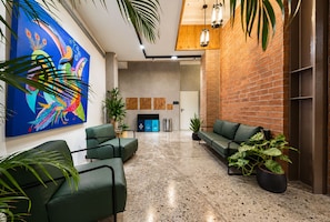 Um hall com assentos verdes, um mural colorido e uma parede de tijolos.