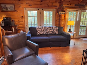 A cabin interior with a leather sofa, a small table with a lamp, and a clock on the wall. - LOG CABIN • 2-bedroom + loft. Access to private association waterfall + courts (Thornton)