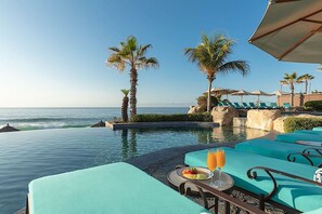 A poolside area with lounge chairs, a table with a fruit platter and drinks, and a view of the ocean. - Cozy 1-bedroom hotel suite in Hacienda Del Mar Los Cabos (Cabo San Lucas)