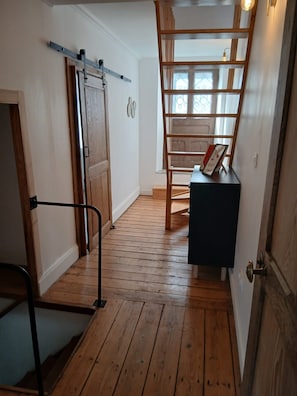 Una escala de fusta amb barana, una porta amb mecanisme de lliscar i una taula petita amb un marc de foto.