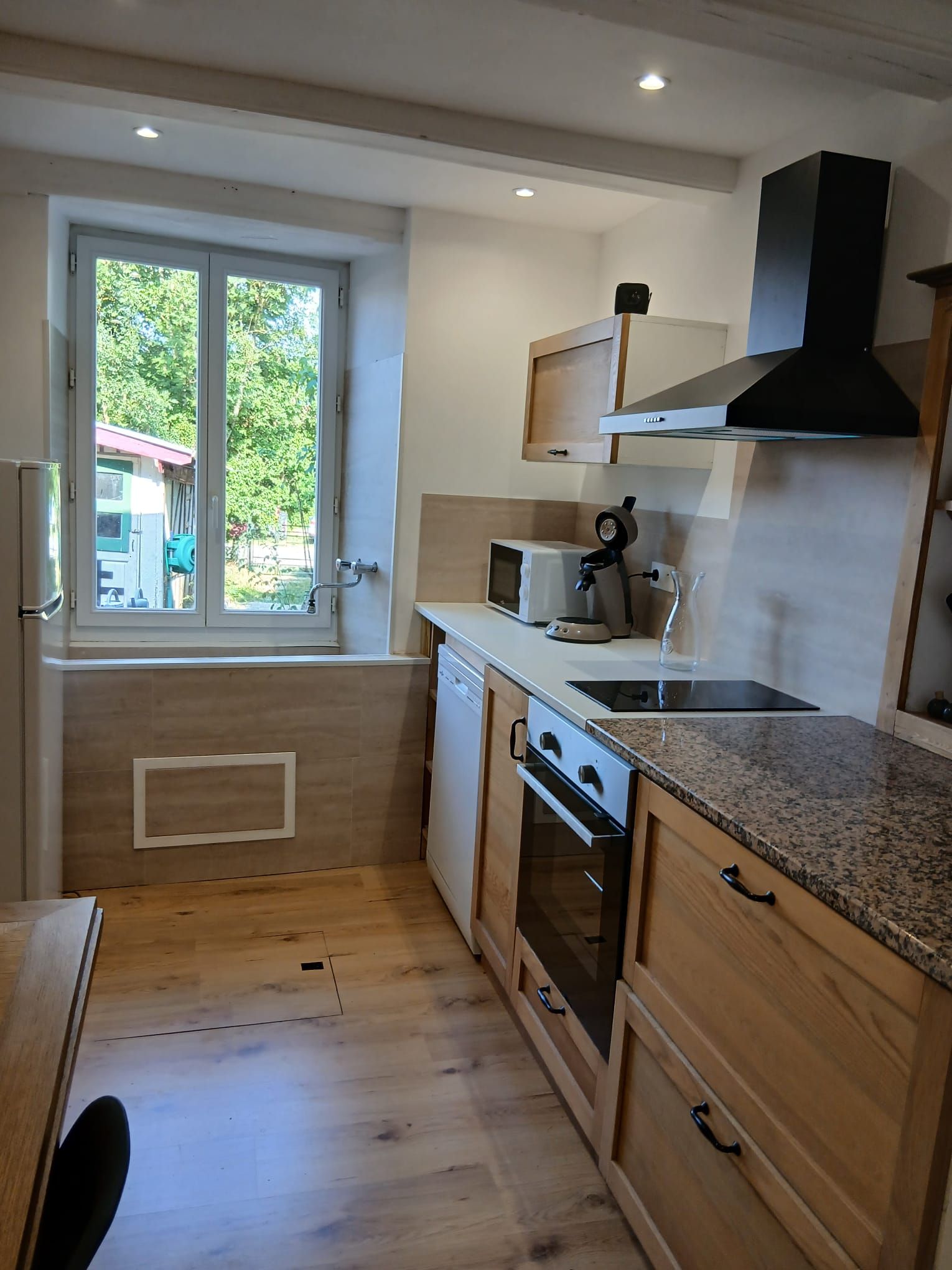 Een kleine keuken met raam, een magnetron, een fornuis en houten kastjes.