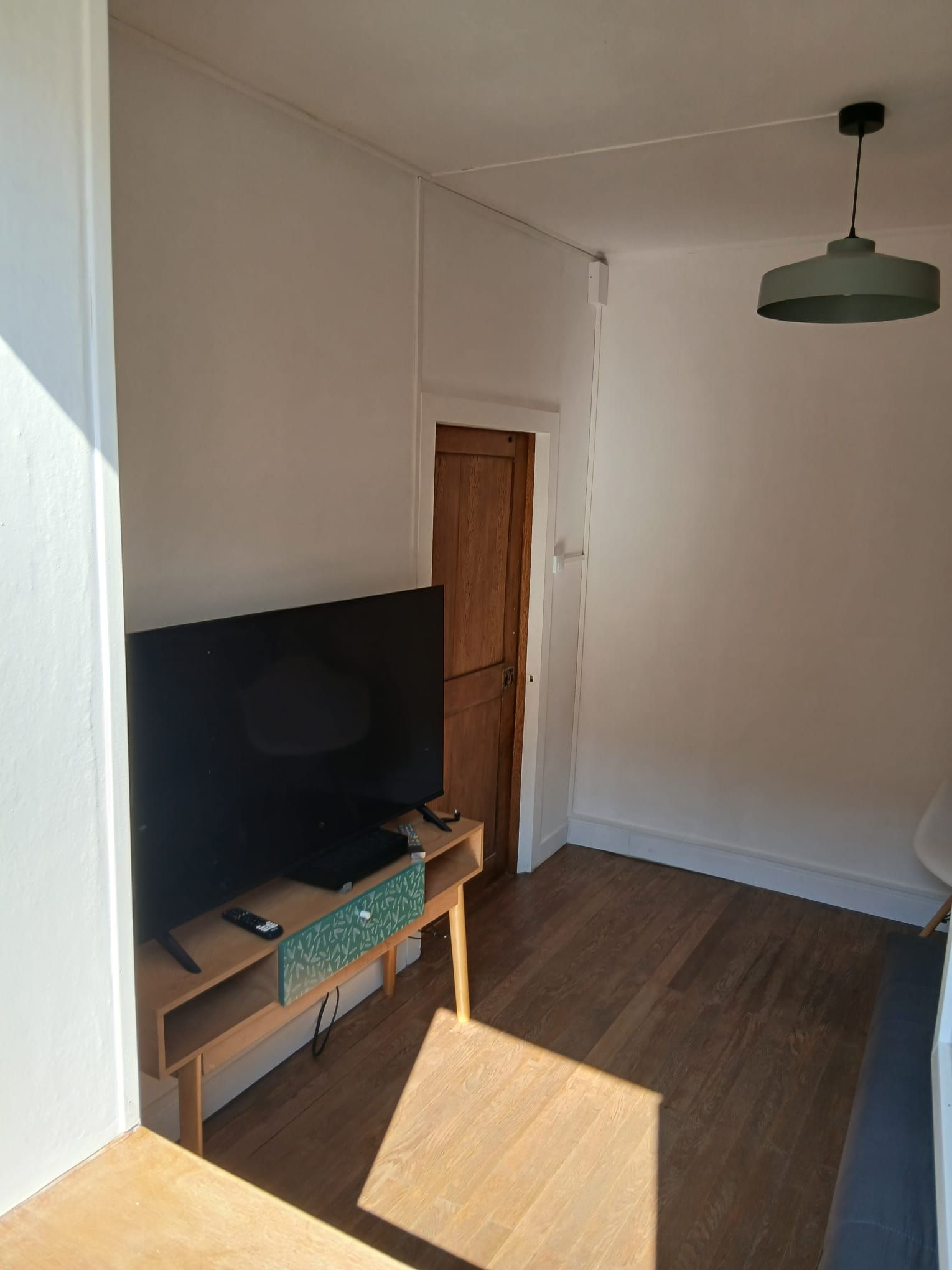 Quarto com televisão sobre apoio de madeira, uma porta e luminária pendente.