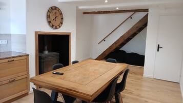 Un coin repas avec une table et des chaises en bois, une horloge au mur et un escalier menant à un niveau supérieur.