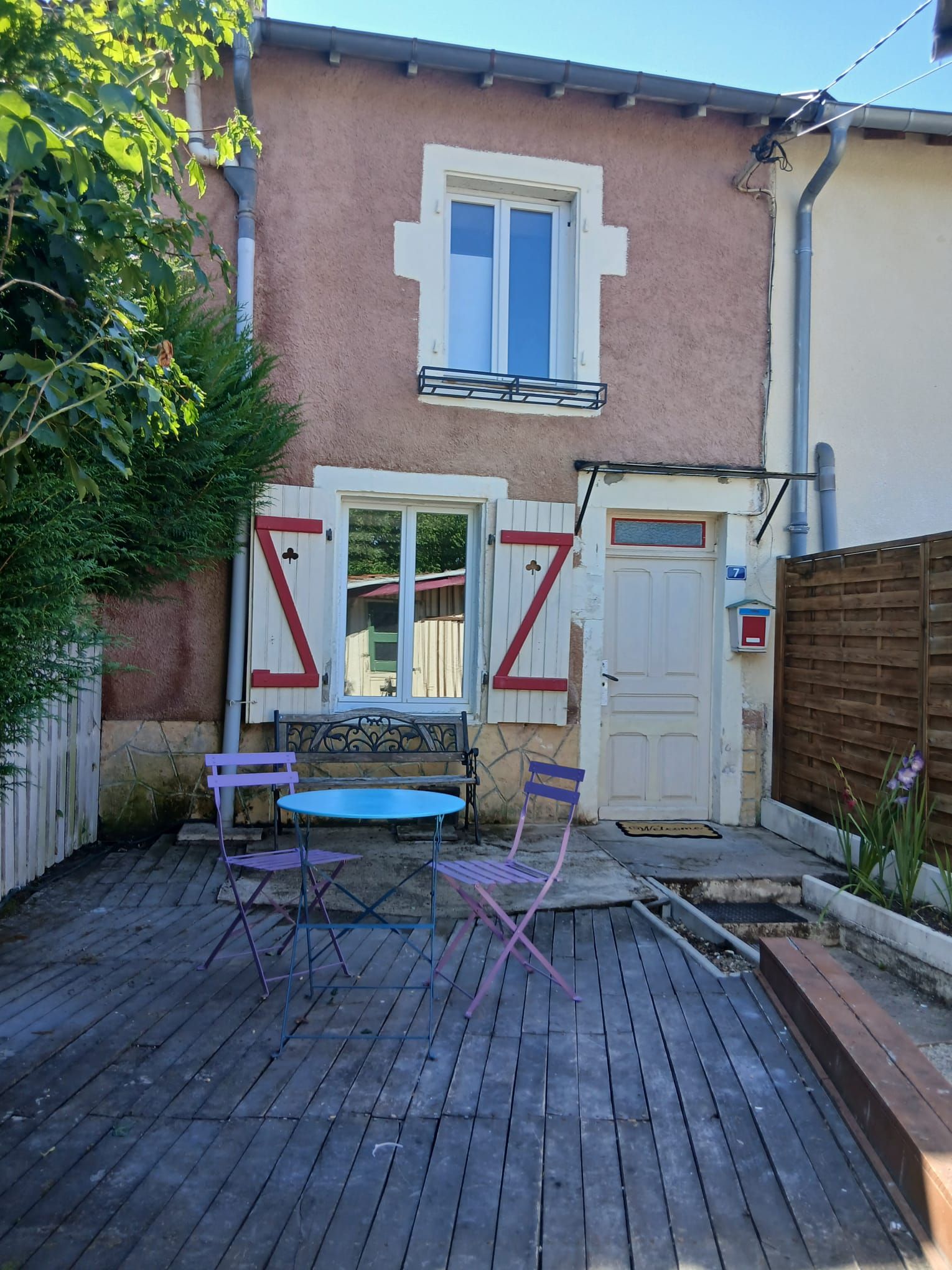 A patio with a table and chairs, a wooden fence, and a house with a window and door.