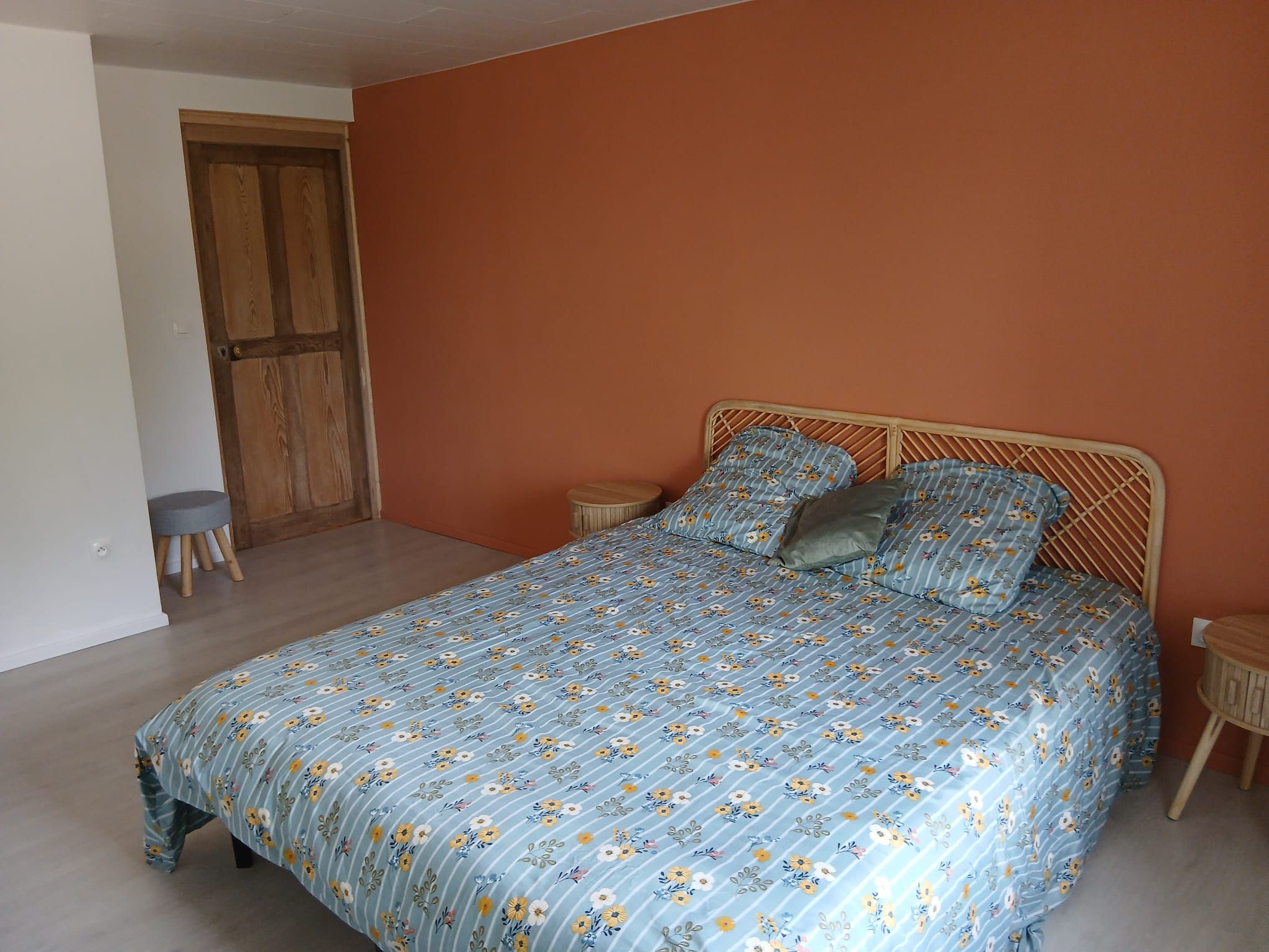 Quarto com cama, porta de madeira e um banquinho.
