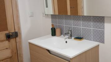 A bathroom with a wooden door, a white sink, a mirror, and patterned tiles.