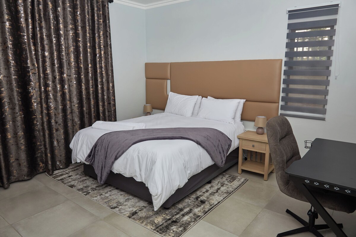 A bedroom with a bed, bedside tables, a desk, and a window with blinds.