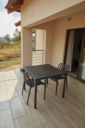 An outdoor patio with a table and chairs, a view of the surrounding landscape, and a building entrance. - Mountain Drive Apartments (Mbabane)