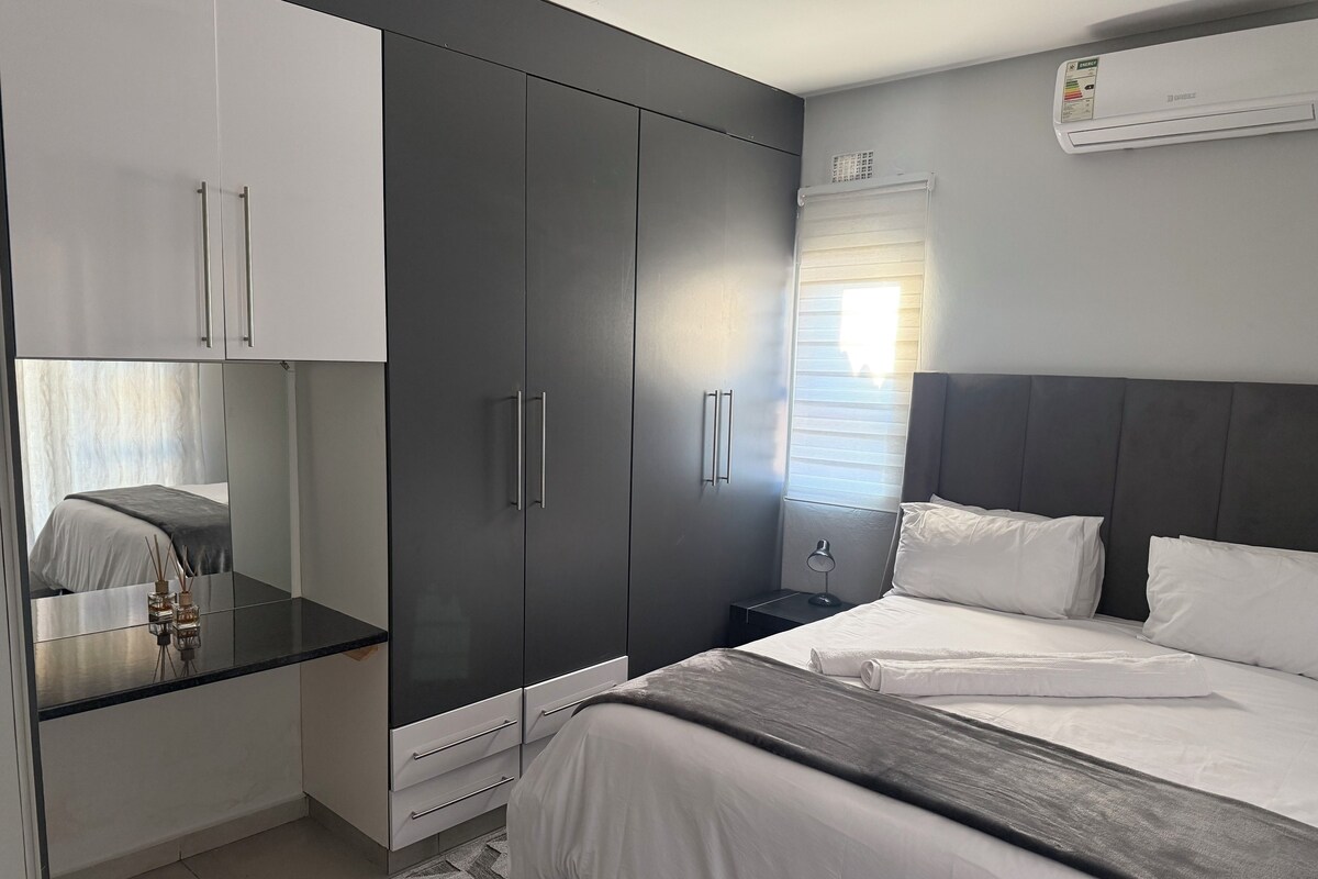 A modern bedroom with a bed, bedside table, wardrobe, and an air conditioning unit.