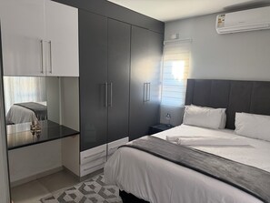 A modern bedroom with a bed, bedside table, wardrobe, and an air conditioning unit. - Mountain Drive Apartments (Mbabane)
