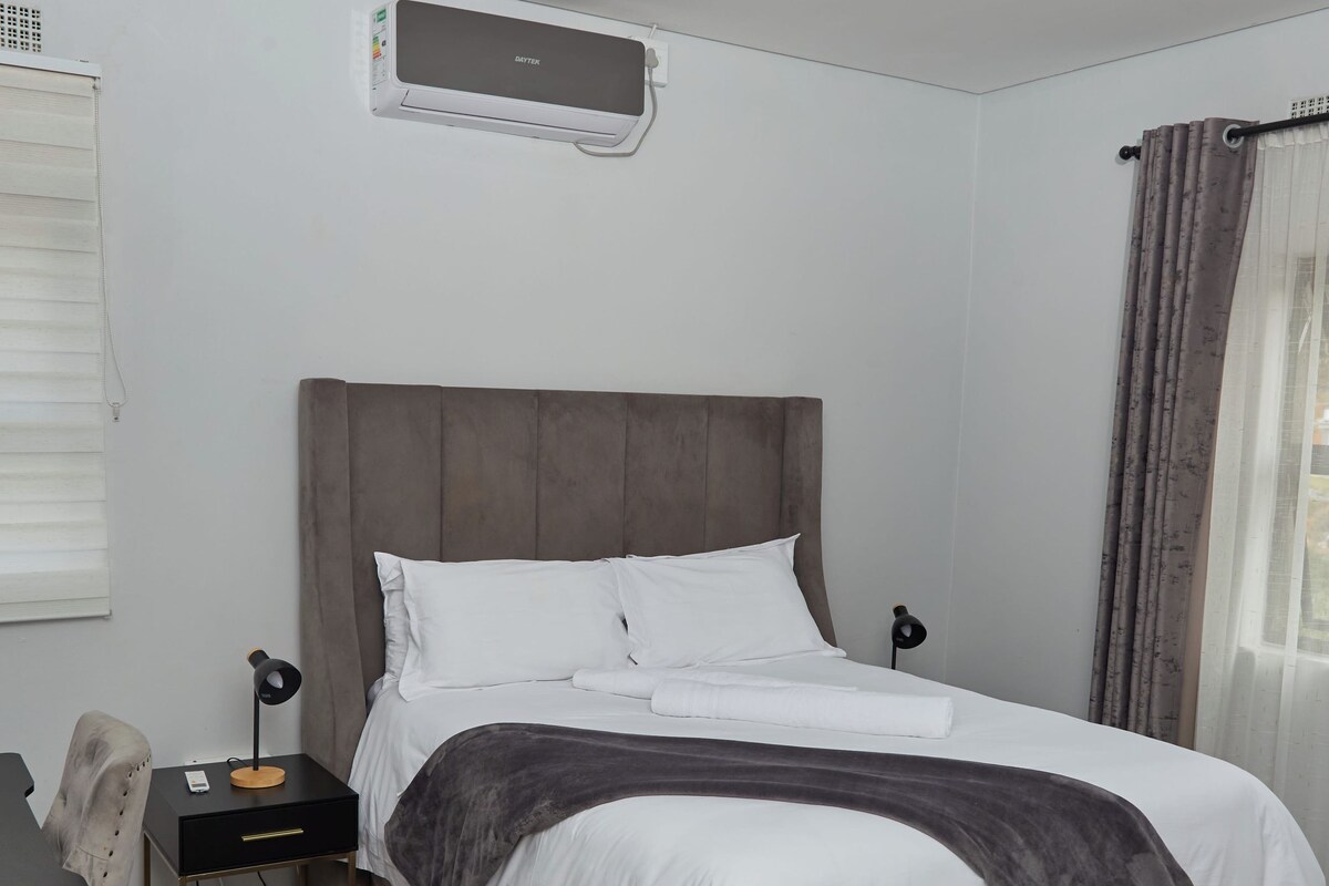A bedroom with a bed, bedside table, chair, desk, and a window with curtains.