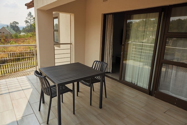 A balcony with a table and chairs, a sliding glass door, and a view of the outdoors. - Mountain Drive Apartments (Mbabane)
