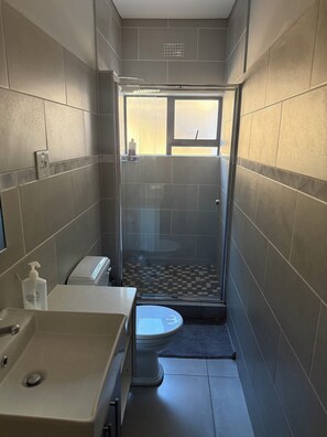 A compact bathroom with a shower, toilet, and sink. - Mountain Drive Apartments (Mbabane)