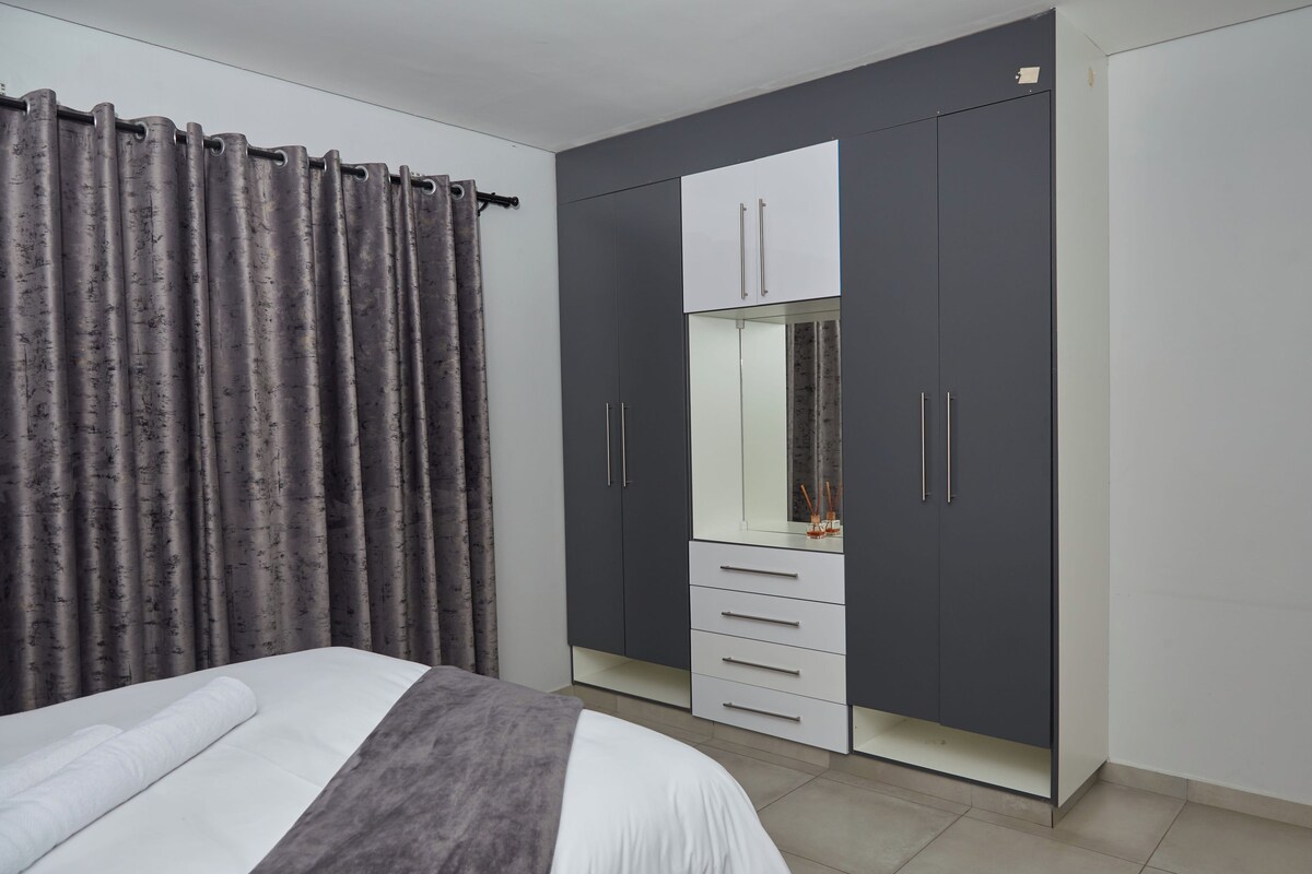 A bedroom with a bed, a wardrobe with a mirror, and grey curtains.