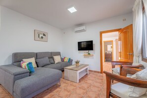 A living room with a grey sofa, a wooden coffee table, a TV, and an open door leading to a bathroom. - Vrbo Property (Coin)