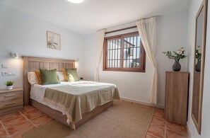 A bedroom with a bed, bedside tables, a nightstand, a window with curtains, and a potted plant. - Vrbo Property (Coin)