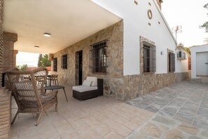 An outdoor patio with wicker furniture, a stone wall, and a covered area with a white ceiling. - Vrbo Property (Coin)